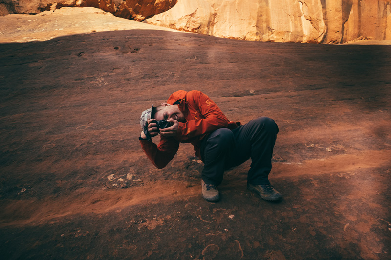 Brian crouching with a camera on red sandstone
